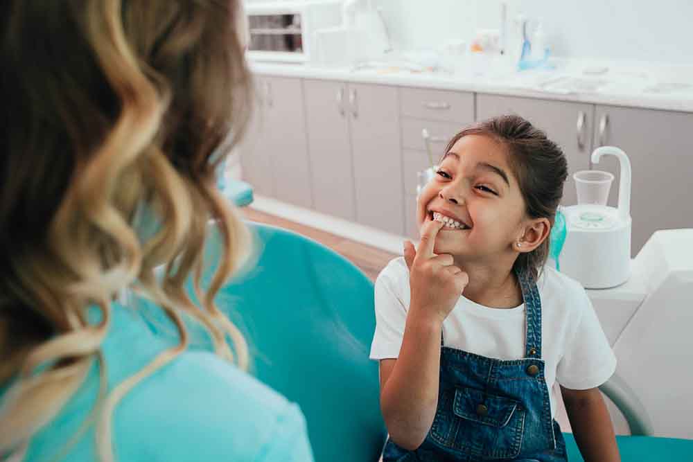Young girl smiling and pointing to her teeth during a pediatric dental visit